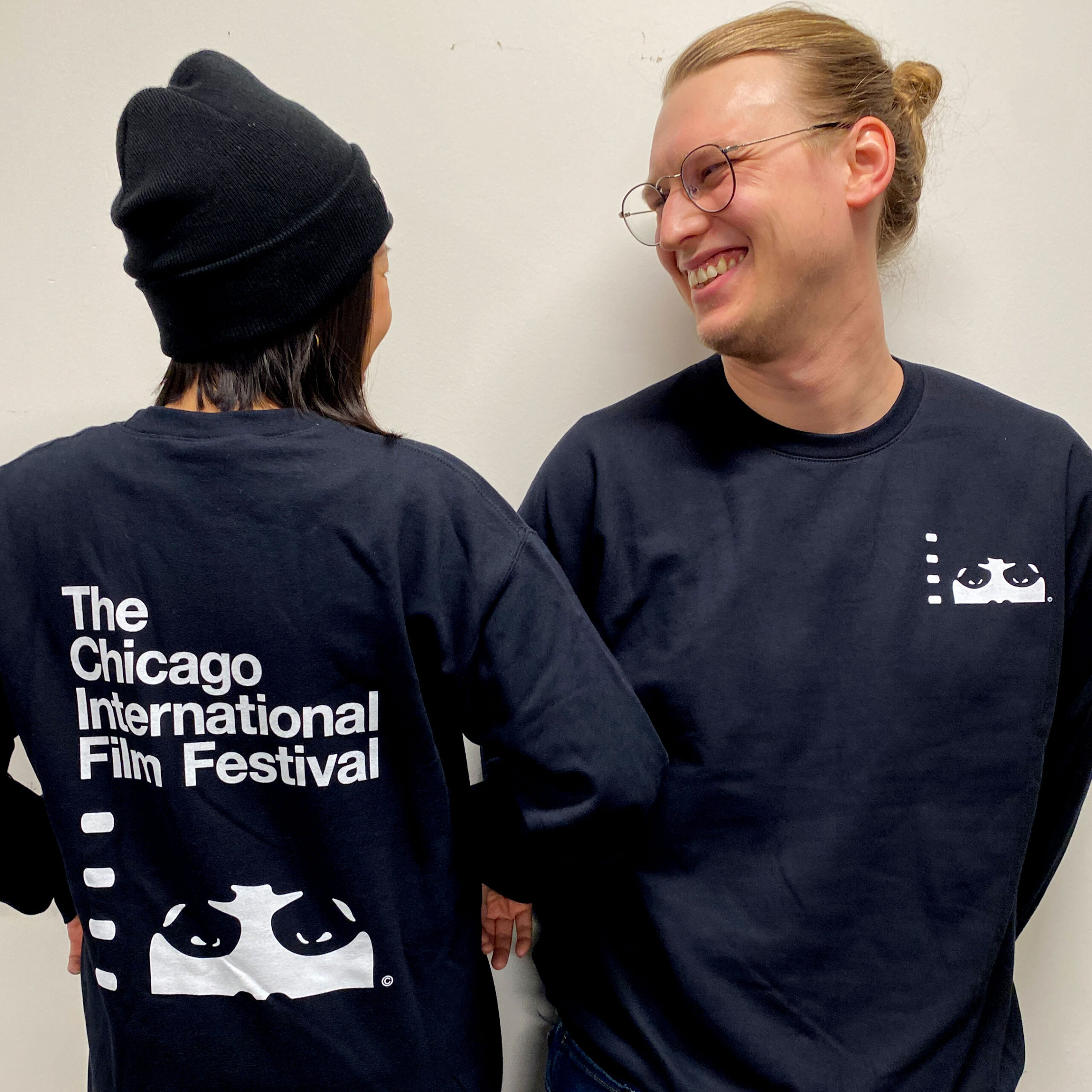 Two people wearing black Festival-branded sweatershirts and a cap